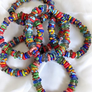 May include: A stack of colorful bracelets made with glass beads. The beads are a mix of red, blue, green, and brown. The bracelets are arranged in a circle.