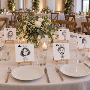 May include: A set of white square place cards on small wooden easels, each featuring a black and white caricature illustration of a person and their name, including Kasia, Anna, Tomasz, Piotr, and Magda, arranged on a table with plates and glasses.