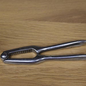 Könnte beinhalten: Ein silberner Nussknacker aus Metall mit einem strukturierten Griff und einem abgerundeten Griff.