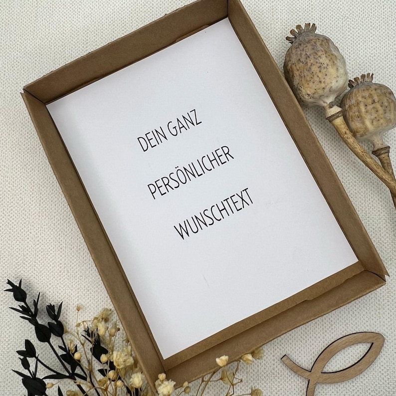 May include: A brown cardboard frame with a white card inside. The card has the text "DEIN GANZ PERS&Ouml;NLICHER WUNSCHTEXT" printed on it.