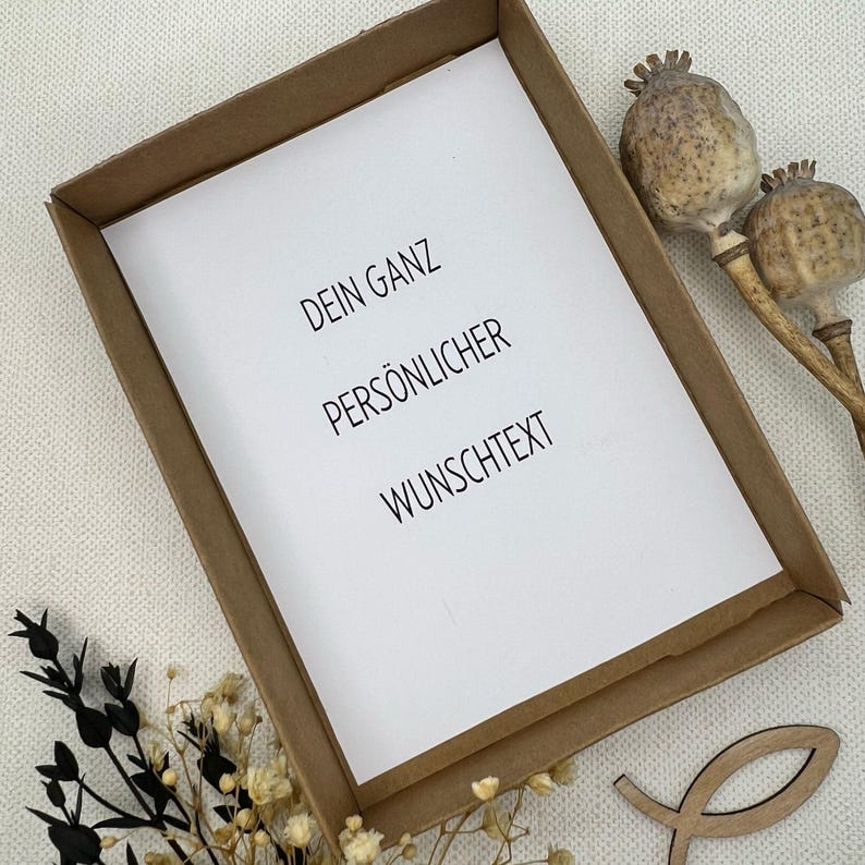 May include: A brown cardboard frame with a white card inside. The card has the text "DEIN GANZ PERS&Ouml;NLICHER WUNSCHTEXT" printed on it.