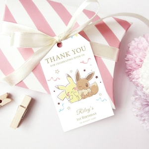 May include: A white thank you tag with a cartoon image of two Pokemon characters, Eevee and Pikachu, with the text "Thank you for celebrating with us" and "Riley's 1st Birthday 22 August 2023".