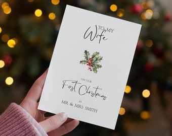 May include: A white Christmas card with the text "To My Wife" and "On Our First Christmas" in elegant script. A holly sprig with red berries is centered. The card is personalized with "Mr & Mrs Smith".