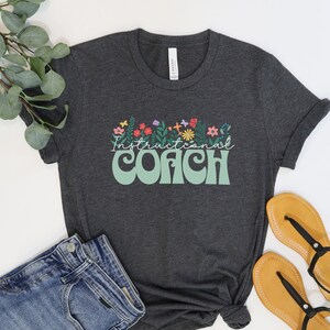 May include: A dark grey t-shirt with a floral design and the text "Instructional Coach" in a retro font.