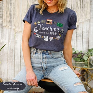May include: A heather navy blue t-shirt with a graphic of vintage classroom technology and the text "Teaching since the 1900s".
