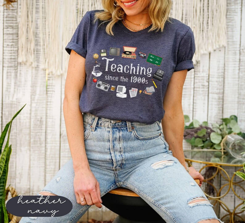 May include: A heather navy blue t-shirt with a graphic of vintage classroom technology and the text "Teaching since the 1900s".