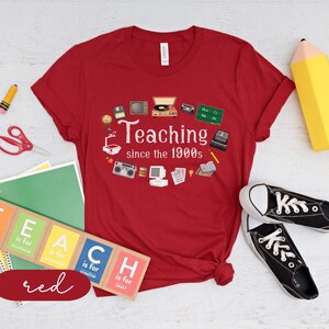 May include: Red t-shirt with a retro design featuring the text "Teaching since the 1900s" and various 1990s-themed icons. The shirt is a great gift for teachers.
