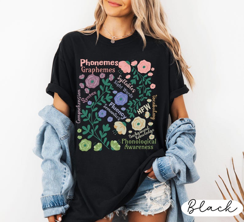 May include: Black t-shirt with a floral design and text related to phonological awareness. The design includes words like "Phonemes," "Graphemes," "Syllables," and "Sight Words" in a floral arrangement. The shirt is a casual wear item.
