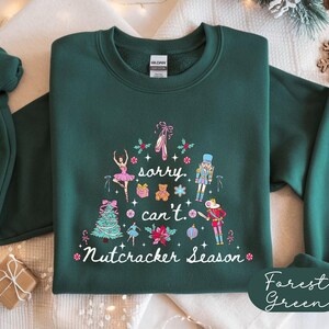 May include: Forest green sweatshirt with a festive Nutcracker Season design. The graphic includes a Christmas tree, ballet dancers, and the text "sorry, can't. Nutcracker Season" in white.