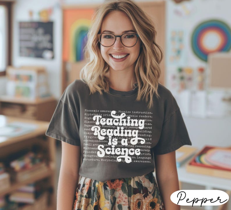 May include: A dark gray t-shirt with the text "Teaching Reading is a Science" in a white, stylized font. The shirt also features smaller text related to reading and education. The person is wearing glasses and a floral skirt.