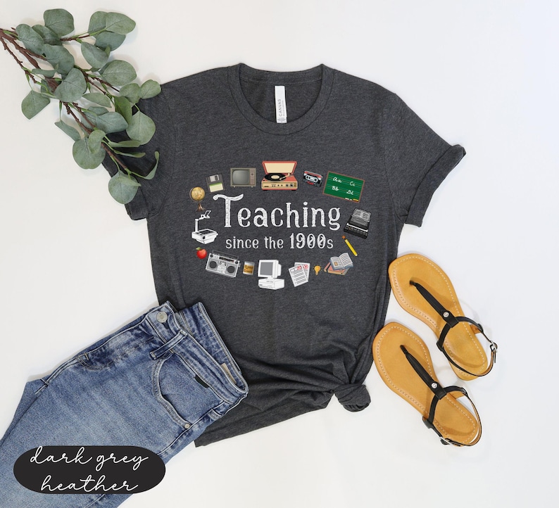 May include: Dark grey heather t-shirt with a white graphic of retro technology icons and the text "Teaching since the 1900s".