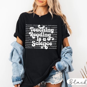 May include: Black t-shirt with the text "Teaching Reading is a Science" in white script. The shirt also features a list of reading-related terms in a smaller font. The shirt is a casual style.