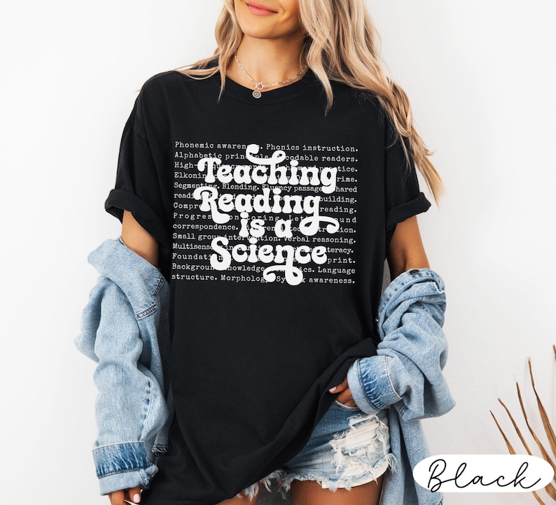 May include: Black t-shirt with the text "Teaching Reading is a Science" in white script. The shirt also features a list of reading-related terms in a smaller font. The shirt is a casual style.
