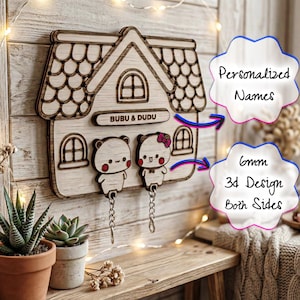 Peut inclure: Porte-clés en bois en forme de maison, avec un design 3D. Il présente deux personnages d'ours et les noms "BUBU & DUDU". Le design comprend le texte "Noms personnalisés" et "Conception 3D de 6 mm des deux côtés".
