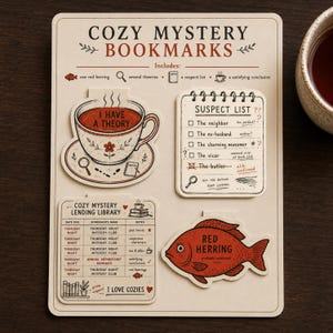 Puede incluir: Un conjunto de cuatro marcapáginas troquelados sobre una tarjeta titulada COZY MYSTERY BOOKMARKS. Los diseños incluyen una taza de té con el texto I HAVE A THEORY, una lista de sospechosos, un registro de biblioteca y un pez rojo etiquetado RED HERRING.