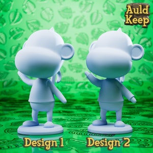 Pode incluir: Dois designs impressos em 3D de um personagem de macaco azul. O macaco está em pé sobre uma base. O primeiro design mostra o macaco de frente com o braço levantado. O segundo design mostra o macaco de costas para o espectador com o braço levantado. O texto "Auld Keep" está no canto superior direito da imagem. O texto "Design 1" está abaixo do primeiro macaco e o texto "Design 2" está abaixo do segundo macaco.