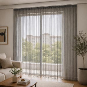 May include: A floor-to-ceiling grey string curtain hanging over a large glass sliding door. The curtain consists of numerous thin, vertical strands that create a semi-transparent, linear texture, allowing light to filter through into the room.