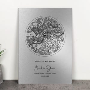 Könnte beinhalten: Silberne Metallplatte mit einer schwarz-weißen Karte von London in einem Kreis. Der Text "WHERE IT ALL BEGAN" und die Namen "Micah & Shane" stehen darunter, zusammen mit dem Datum und dem Ort.