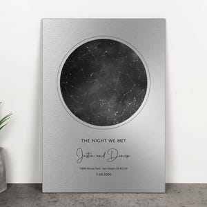 May include: A silver metal plaque featuring a black and white star map within a circular frame. The text "THE NIGHT WE MET" is above the names "Jasta and Denise" and the date "7-16-2005". The location is "1998 Alcala Park, San Diego CA 92110".