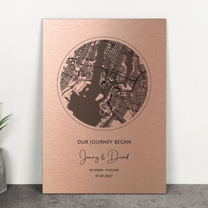 May include: A rectangular, rose-gold metal plaque featuring a circular map of a city, likely New York. The text "OUR JOURNEY BEGAN" is above the names "Jenny & David" and a date and coordinates. A decorative piece.