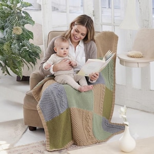 May include: A patchwork knit blanket in shades of gray, green, and tan. The blanket features various textured patterns and is draped over a chair. A woman and a baby are seated in the chair, reading a book.