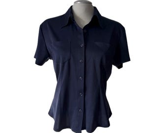 May include: A navy blue short-sleeved button-down shirt with a collared neckline and two chest pockets. The shirt is displayed on a mannequin and has a fitted silhouette. The fabric appears to be a smooth, solid color.