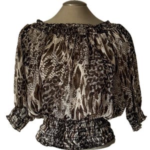 May include: A sheer, off-the-shoulder blouse with a brown and white animal print. The top features a gathered neckline and waist, with three-quarter sleeves. The fabric has a flowing, lightweight appearance.