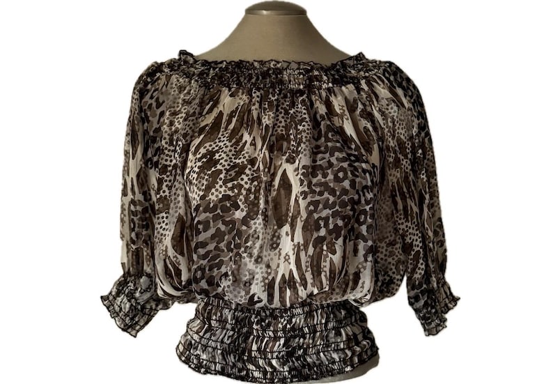 May include: A sheer, off-the-shoulder blouse with a brown and white animal print. The top features a gathered neckline and waist, with three-quarter sleeves. The fabric has a flowing, lightweight appearance.