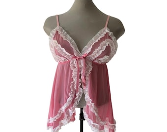 May include: A pink sheer babydoll top featuring thin spaghetti straps, a deep V-neckline, and white ruffled trim along the edges. The garment includes a small pink ribbon bow at the center of the bust and a flowing, semi-transparent fabric.