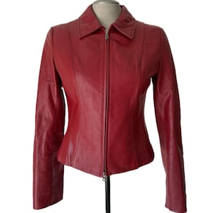 Puede incluir: Chaqueta de cuero roja con cuello y cremallera completa. La chaqueta tiene mangas largas y se exhibe en un maniquí. El cuero parece liso y tiene un ligero brillo.