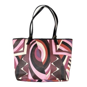 Op de afbeelding: Een tote bag met een geometrisch patroon in tinten roze, bordeaux en crème. De tas heeft zwarte handvatten en een rechthoekige vorm. Het ontwerp bevat abstracte vormen en lijnen, wat een moderne en stijlvolle uitstraling creëert.