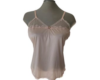 May include: A light beige camisole featuring a V-neckline with sheer dotted mesh fabric and delicate lace trim. The garment includes thin, adjustable shoulder straps and a small decorative bow centered at the neckline, crafted from a smooth fabric.