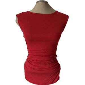 May include: A sleeveless red top featuring a high, rounded neckline and a fitted silhouette. The garment includes horizontal ruching details along the midsection and sides, creating a gathered texture that extends down to the hemline.
