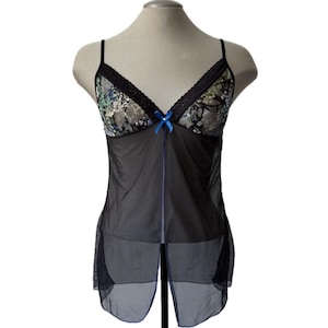 Könnte beinhalten: Schwarzes Dessous-Top mit floralen Spitzendetails auf der Brust und einer kleinen blauen Schleife. Das Top hat dünne Träger und einen transparenten, fließenden Rock. Die Brust zeigt ein Blumenmuster mit grünen und blauen Akzenten.