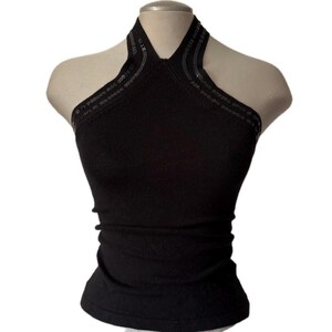 May include: A black halter-neck top featuring a high neckline with decorative black sequin trim along the straps. The garment is sleeveless, form-fitting, and constructed from a solid black fabric, displayed on a neutral-toned mannequin torso.