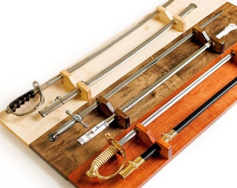 May include: Three swords with metal blades and distinct hilts are mounted horizontally on three separate wooden display boards. The boards feature light, medium, and dark wood finishes, each equipped with two wooden supports to hold the swords.