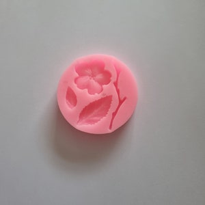 May include: Pink silicone mould with a flower and leaves design. The mould is round and has a smooth surface.