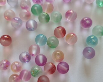 May include: A collection of colorful, translucent beads with a frosted finish. The beads are various shades of pink, purple, blue, green, and red. They have a subtle shimmer and sparkle.