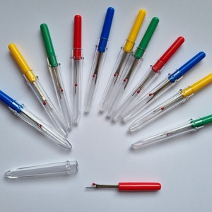 May include: A collection of ten colourful thread snippers with clear plastic handles. The snippers are arranged in a fan shape on a white surface.
