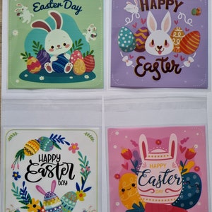 May include: Four different Easter-themed cards featuring bunnies and eggs. The cards are in a clear plastic bag. The first card is green with a white bunny holding an egg. The second card is purple with a white bunny and the text "Happy Easter". The third card is white with a floral wreath and the text "Happy Easter Day". The fourth card is pink with a white bunny and the text "Happy Easter Day".