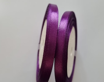 May include: Two spools of purple satin ribbon. The ribbon is wound around white spools.