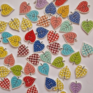 Op de afbeelding: Assortiment van houten hartvormige knopen in verschillende kleuren en patronen, waaronder stippen, ruitjes en bloemenpatronen.