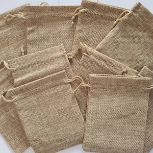 Puede incluir: Un grupo de 12 pequeñas bolsas de arpillera de color marrón con cordón. Las bolsas están hechas de un tejido natural tejido y tienen un aspecto rústico y terroso.