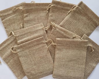 May include: A group of 12 small, brown burlap drawstring bags. The bags are made of a natural, woven fabric and have a rustic, earthy look.
