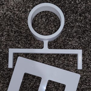 May include: A white, three-piece, 3D-printed object. The top piece is a ring with a stem. The middle piece is a horizontal bar with two right angles. The bottom piece is a rectangle with two rectangular cutouts.
