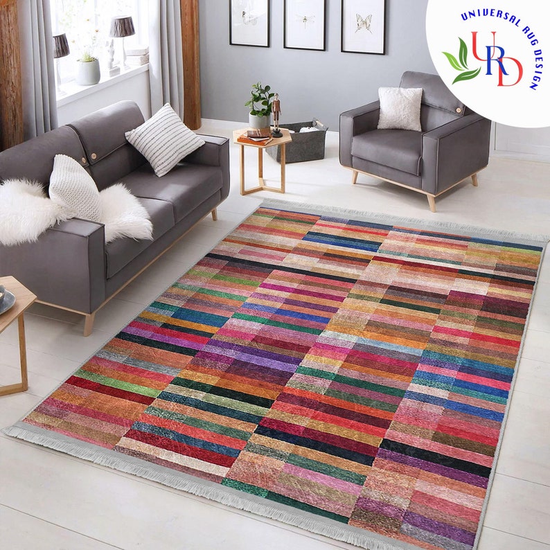 May include: A colorful rectangular rug with a geometric pattern of horizontal stripes in various shades of red, orange, yellow, green, blue, purple, and brown. The rug has a white fringe border.