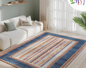 May include: A blue and beige patterned area rug with a dark blue border. The rug is laid out on a light wood floor in a living room setting with a white couch.