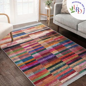 May include: Multicolored area rug with a geometric pattern of horizontal and vertical stripes. The rug has a fringe border and is made of a soft, woven material.