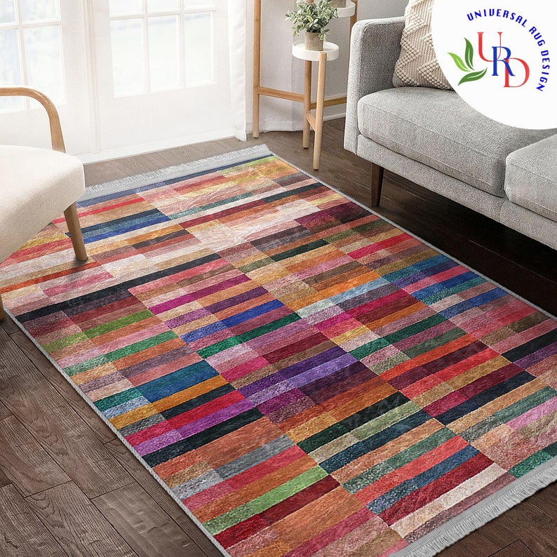 May include: Multicolored area rug with a geometric pattern of horizontal and vertical stripes. The rug has a fringe border and is made of a soft, woven material.