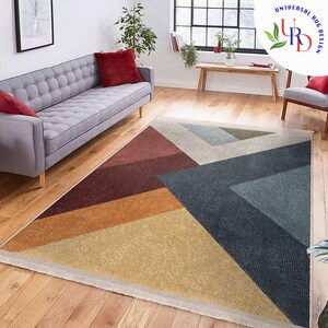 May include: Geometric area rug with a modern design. The rug features a triangular pattern with sections of red, orange, yellow, blue, and gray. The rug is placed on a hardwood floor in a living room setting.